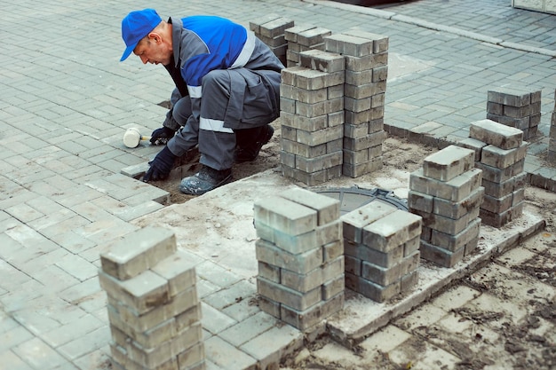 Metselaar legt straatstenen buiten Werkende man voert landschapsarchitectuur uit Bouwer legt trottoir aan met stenen blokken