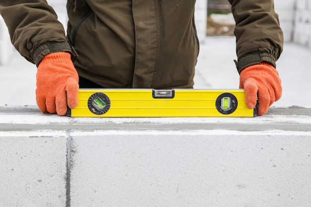 Metselwerker maakt beton Niveau wordt gebruikt bij het leggen van stenen om de gorizontaliteit te controleren, man bouwt nieuw huis van wit gassilicaatblok