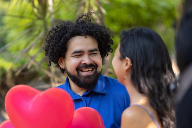 Mexicaans jong latijns koppel lachend en pratend op valentijnsdag met rode hartvormige ballonnen