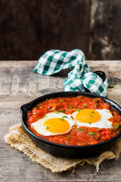 Mexicaans ontbijt: Huevos rancheros in ijzeren koekenpan op houten tafel