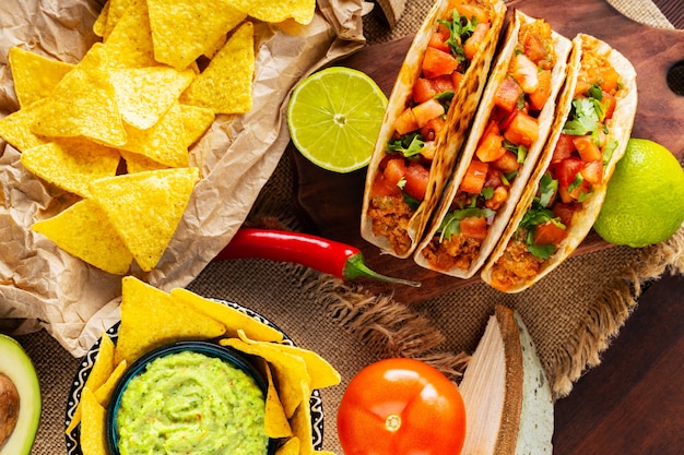 Mexicaans voedselpanorama. nacho's, guacamole, taco's en ingrediënten op houten planken. variatie van mexicaanse taco en nacho tortillachips. plat leggen. bovenaanzicht