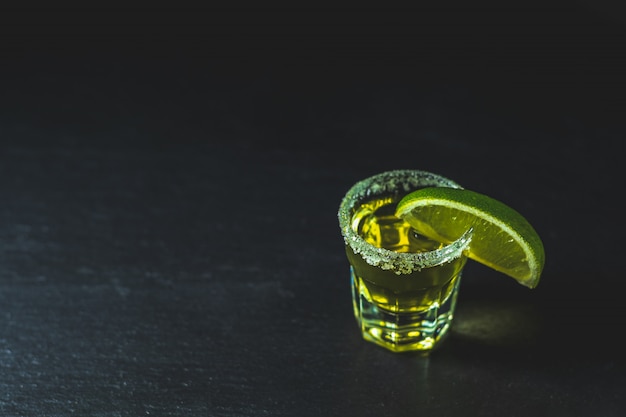 Mexicaanse gouden Tequila geschoten met limoen en zout op zwarte stenen tafel oppervlak