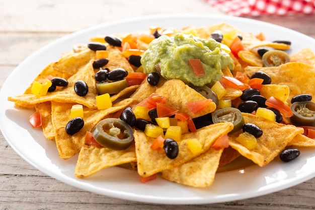 Mexicaanse nachos tortillachips met zwarte bonen, guacamole, tomaat en jalapeno op houten tafel