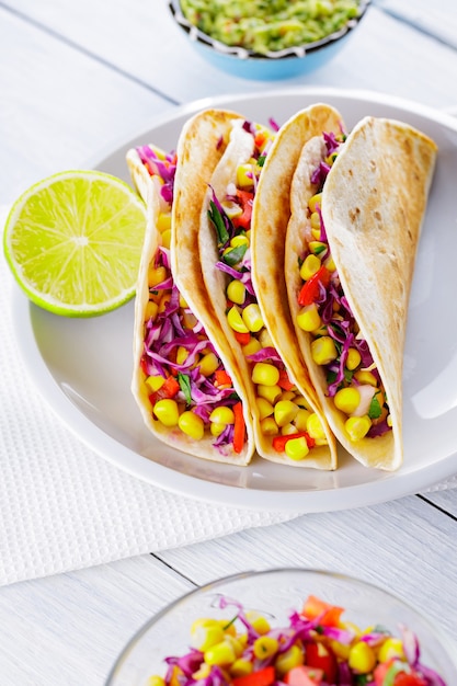 Mexicaanse taco's met verschillende groenten en guacamole op witte borden. Veganistische taco's met maïs, paarse kool en tomaten op een witte plaat. Mexicaanse keuken