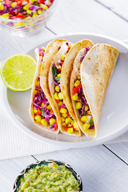 Mexicaanse taco's met verschillende groenten en guacamole op witte borden. Veganistische taco's met maïs, paarse kool en tomaten op een witte plaat. Mexicaanse keuken