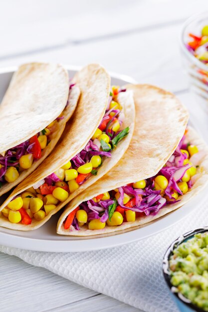 Mexicaanse taco's met verschillende groenten en guacamole op witte borden. Veganistische taco's met maïs, paarse kool en tomaten op een witte plaat. Mexicaanse keuken