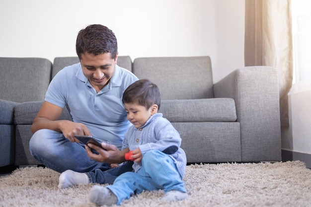 Mexicaanse vader en zoon die telefoon op tapijt thuis bekijken