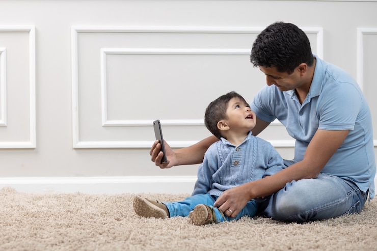 Mexicaanse vader en zoon die telefoon op tapijt thuis bekijken