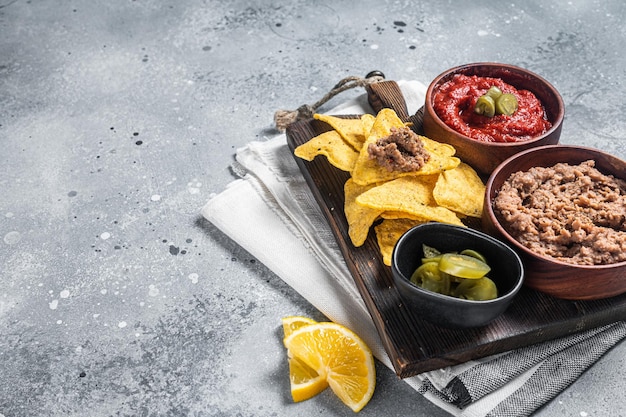 Mexican appetizer corn chips nachos with fried minced meat\
tomato sauce and jalapeno gray background top view copy space