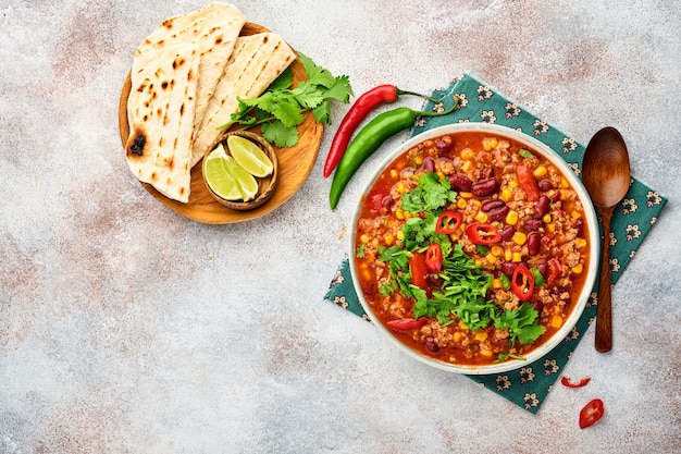 Mexican black bean soup with minced meat, tomato, cilantro,\
avocado and vegetables stew on a light grey slate, stone or\
concrete background. traditional mexican dish. top view with copy\
space.