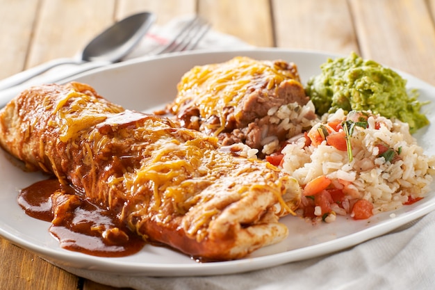 Foto piatto di burrito messicano con salsa enchilada rossa, fagioli fritti, riso e guacamole