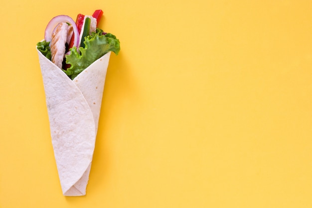 Mexican chicken fajita with peppers lettuce and onion on yellow table copy space