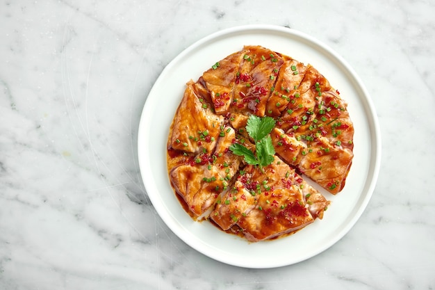 Mexican cuisine dish - tostada with salmon, sweet and sour sauce, onions, cilantro, served in a white plate on a marble table. Close up, selective focus