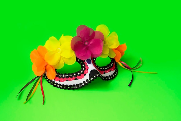 Mexican face mask with flowers and ribbons on the green background. Day of the dead concept