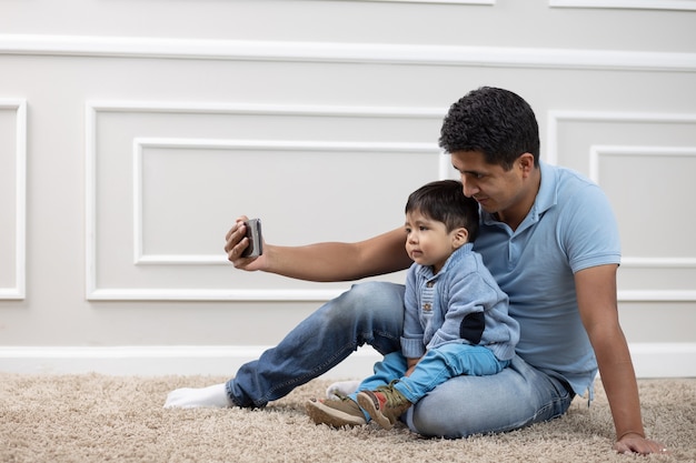 Mexican father and son looking at phone on carpet at home