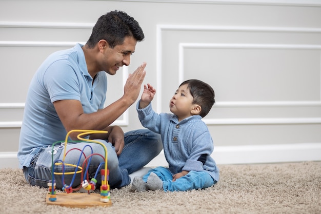 Mexican father and son playing on carpet at home, high five