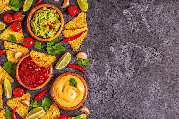 Photo mexican food background: guacamole, salsa, cheesy sauces with ingredients on black background, top view.