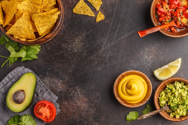 Photo mexican food concept. nachos - yellow corn totopos chips with various sauces in wooden bowls: guacamole, cheese sauce, pico del gallo, frame of food, top view, copy space.