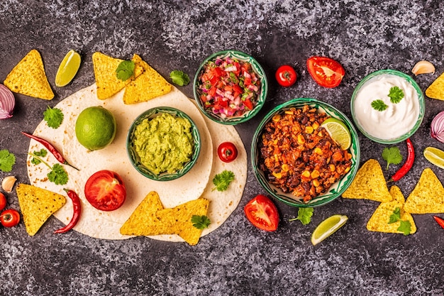 Mexican food concept: tortillas, nachos with guacamole, salsa, chili con carne, top view.