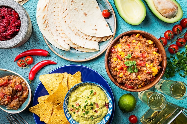 Mexican food mix nachos, fajitas, tortilla, guacamole and salsa sauces and ingredients over blue surface. Top view