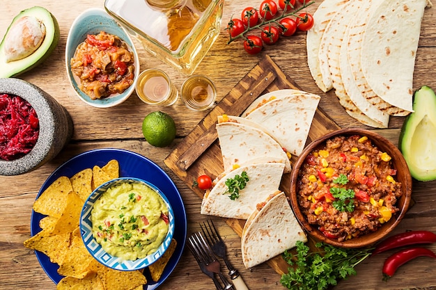 Mexican food mix nachos, fajitas, tortilla, guacamole and salsa sauces and ingredients over wooden surface. Top view