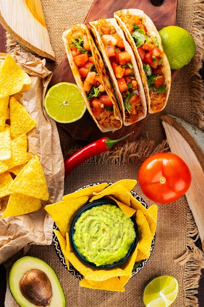 Mexican food table with nachos, guacamole, tacos and\
ingredients. mexican taco and nacho tortilla chips on wooden\
boards. hispanic mexican food