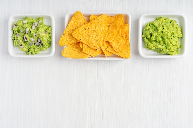 Mexican guacamole dipping sauce made of avocado and with addition of red onion with nacho chips