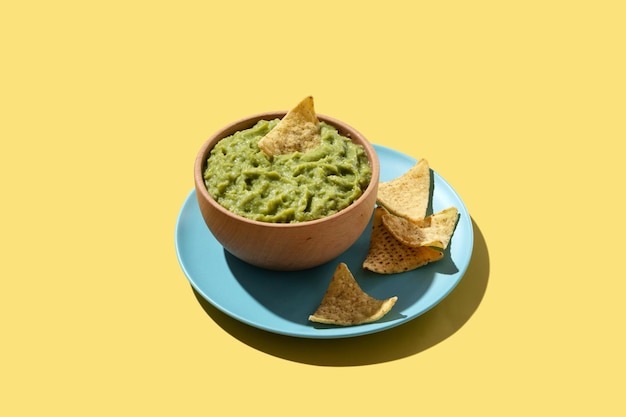 Mexican guacamole with nacho chip in wooden bowl on yellow background