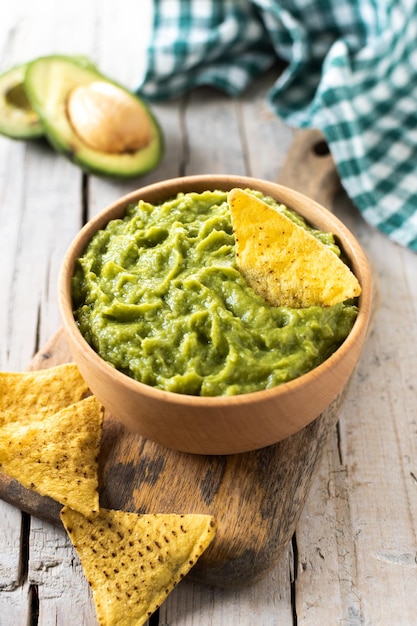 Mexican guacamole with nacho chip in wooden bowl