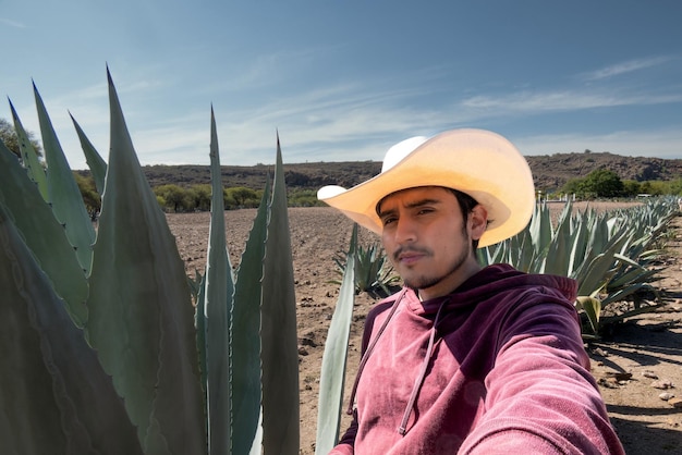 Foto un messicano latino con un cappello che lavora nel campo circondato da agave di pulque e tequila