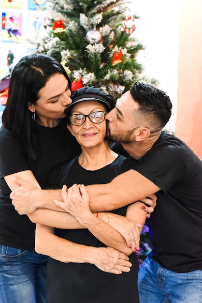 Mexican married couple kissing therir mother against christmas tree