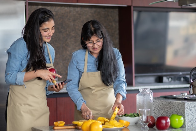 mexican mother and daughter cooking in kitchen looking the recipe on smartphone