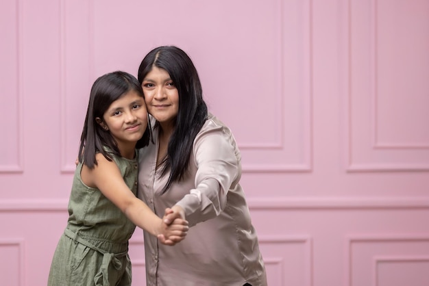 Mexican mother and daughter hugging on pink background isolated