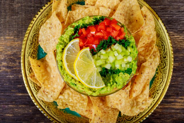 Mexican nacho chips and guacamole dip in bowl on wooden background