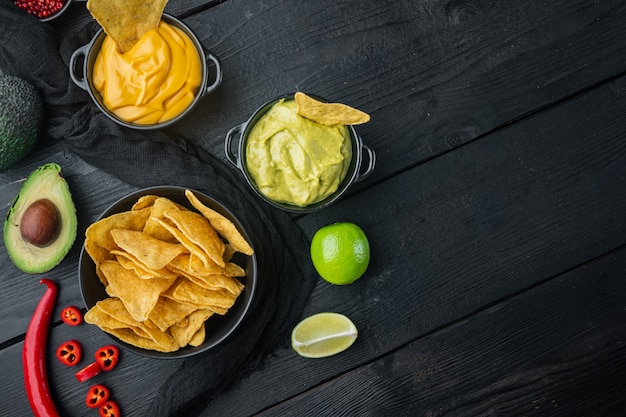 Chips di nachos messicani con formaggio e salse guacamole, sul tavolo di legno nero, vista dall'alto o piatto