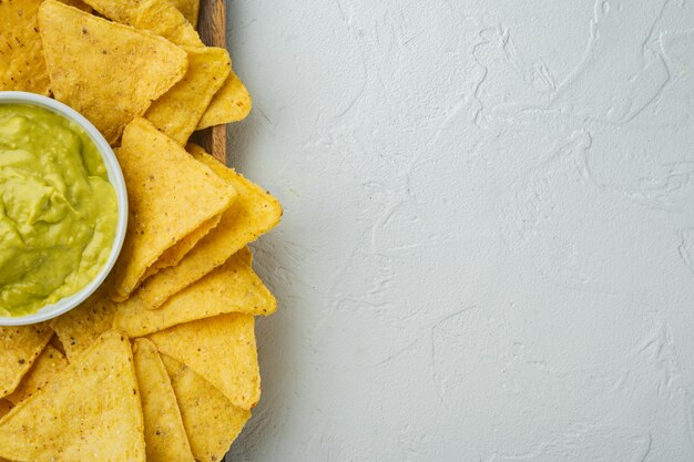 Mexican nachos chips with cheese and guacamole sauces, on white table, top view or flat lay