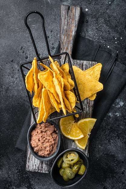 Mexican nachos corn chips with Chili con carne and jalapeno in a basket Black background Top view