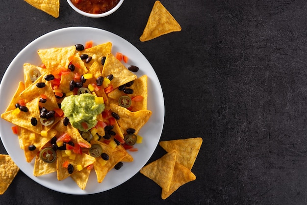 Mexican nachos tortilla chips with black beans guacamole tomato and jalapeno on black background