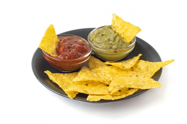 Mexican nachos tortilla chips with guacamole and salsa in dark plate. Isolated on white background
