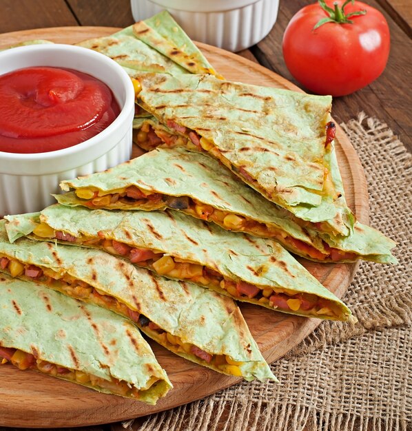 Mexican Quesadilla sliced with vegetables and sauces on the table