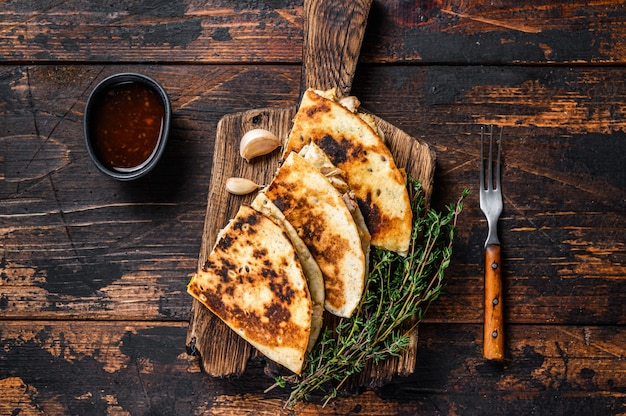 Mexican quesadilla with chicken, paprika, cheese and cilantro\
on wooden cutting board on wooden table. top view.