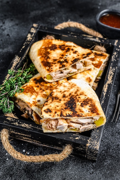 Mexican quesadilla with chicken, tomato, corn and cheese on black table. Top view.