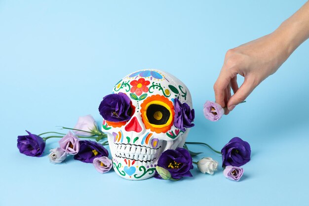 Mexican skull flowers and hand on blue background