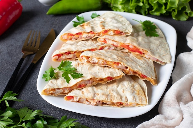 Mexican snack quesadilla from tortilla with bacon chicken cheese and pepper in white plate on gray background