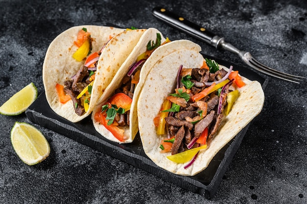 Mexican tacos shells with beef meat, onion, tomato and sweet pepper. Black background. Top view.