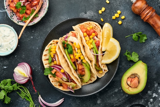 Mexican tacos with grilled chicken, avocado, corn kernels,\
tomato, onion, cilantro and salsa at black stone table. traditional\
mexican and latin american street food. top view.