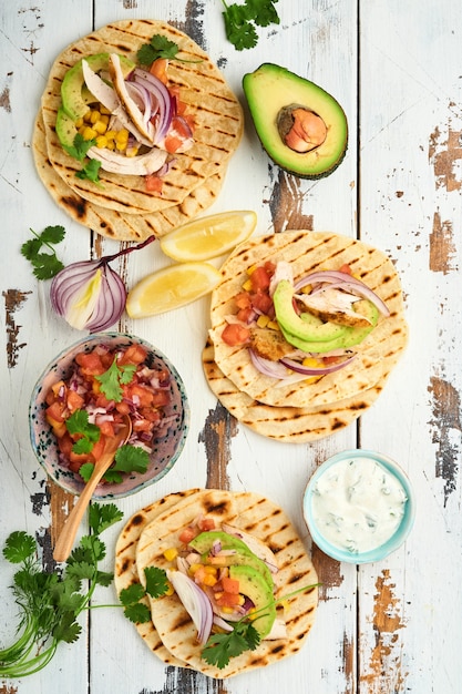 Mexican tacos with grilled chicken, avocado, corn kernels, tomato, onion, cilantro and salsa old white wooden table. Traditional Mexican and Latin american street food. Top view.