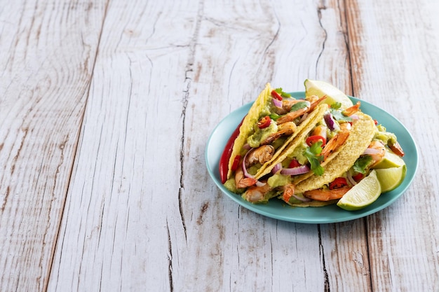 Mexican tacos with shrimpguacamole and vegetables on wooden table