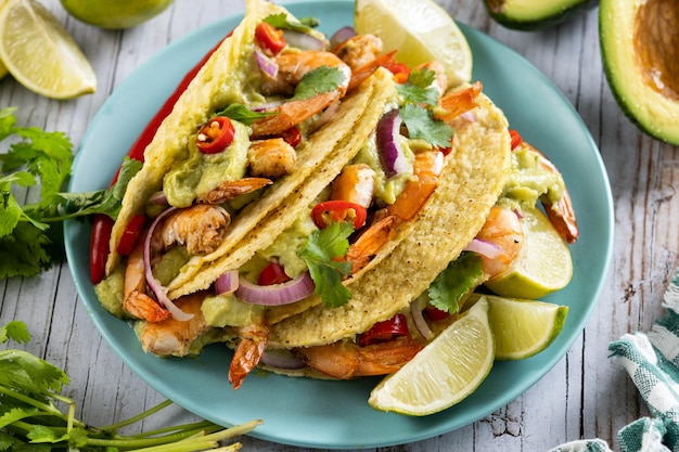 Mexican tacos with shrimpguacamole and vegetables on wooden table