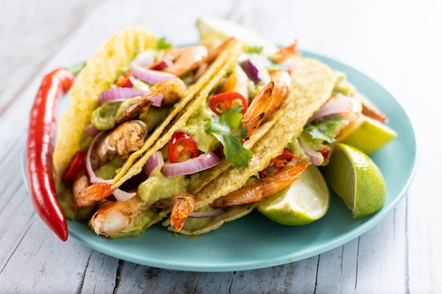 Mexican tacos with shrimpguacamole and vegetables on wooden table